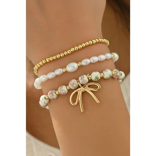 Gold, white pearl, and pink floral beaded triple layer bracelet set with bow charm shown on model's wrist for styling