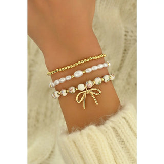 Triple layer bow charm beaded bracelet set with gold beads, pearls, and floral beads shown on wrist with fluffy cream sweater