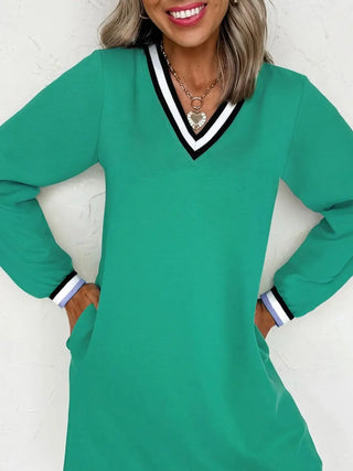 Woman wearing green varsity V-neck dress with striped cuffs and pockets, smiling and posing against white background.