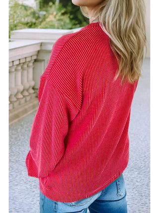 Woman wearing a red ribbed knit sweatshirt from the back, showing relaxed fit and long sleeves, worn with jeans.