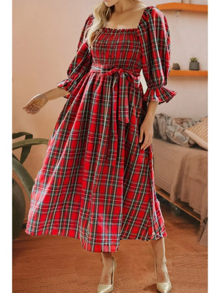 Woman wearing red plaid holiday midi dress from LDC with smocked bodice, bow waist, and puff sleeves, standing indoors.
