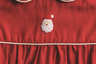 Red poplin baby bubble with hand-embroidered Santa, Peter Pan collar, and white piping—perfect for holiday photos and gatherings.