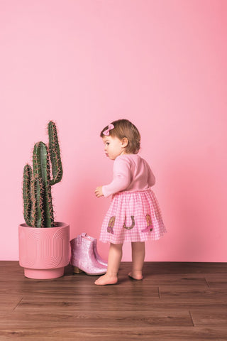 Toddler girl in Mud Pie Western Sequin Dress with pink gingham skirt and sequin boots and horseshoes, styled with pink bow.