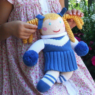 Little girl holding blue knit cheerleader doll with yellow yarn pigtails, striped socks, and soft plush baby toy design