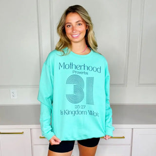 Model wearing mint Proverbs 31 Motherhood sweatshirt with Proverbs 31 graphic standing in bright room with drawers behind her.
