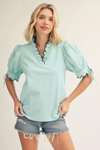Front close view of aqua blouse with scalloped V neckline, contrast trim, and scalloped puff sleeve detail styled with shorts