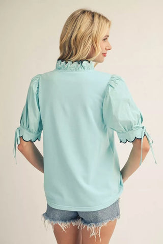 Back view of aqua blouse with scalloped collar, puff sleeves, and tie cuff detail paired with denim shorts