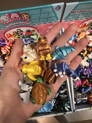 Hand holding assorted Zorbitz Twiddle-Itz 3D printed metallic animal fidget toys, including turtle, duck, chicken, and more.