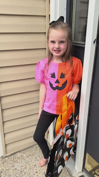 Video showcasing a Banana Split short-sleeve sweatshirt for kids, featuring a half-pink, half-orange design with a black jack-o'-lantern face.